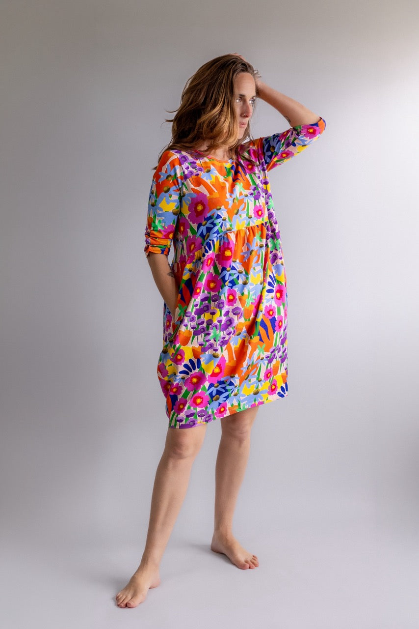 Full-length view of a woman wearing the REN Dress in Bloomcore against a grey studio background.