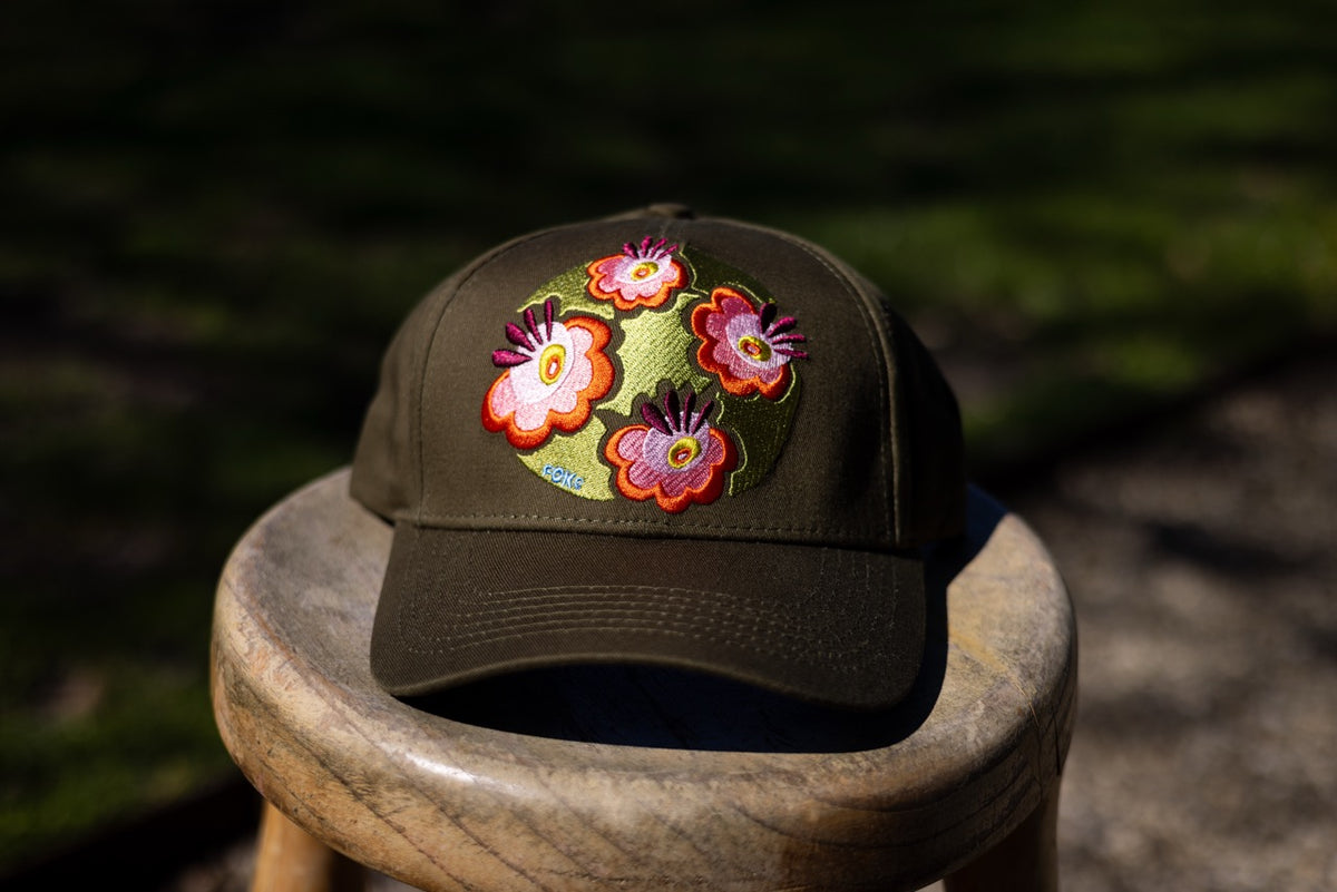 Front view of the Olive FOKE trucker cap, with four colourful embroidered flowers above the curved peak.