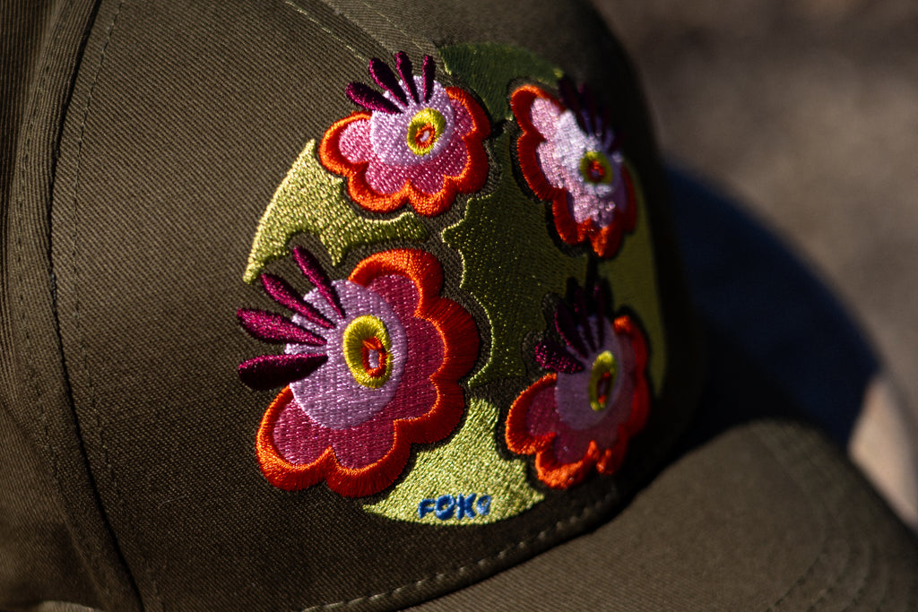 Close-up of colourful FOKE floral embroidery on an olive cap.
