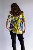 Woman wearing the colourful yellow FOKE artist tee, back view showing the all-over original print.