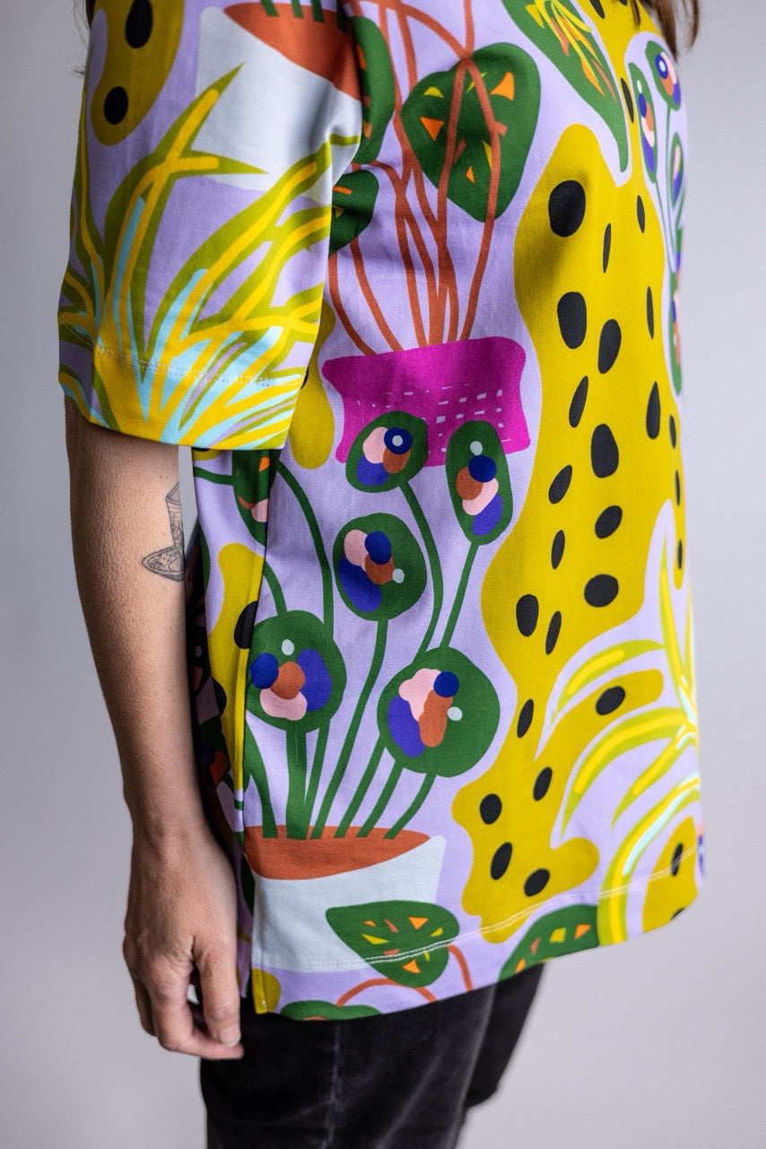 A close-up of a person wearing a short-sleeve t-shirt with a vibrant, multicolored abstract pattern featuring yellow, green, pink, orange, and purple shapes on a light background.
