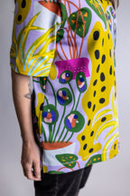 A close-up of a person wearing a short-sleeve t-shirt with a vibrant, multicolored abstract pattern featuring yellow, green, pink, orange, and purple shapes on a light background.