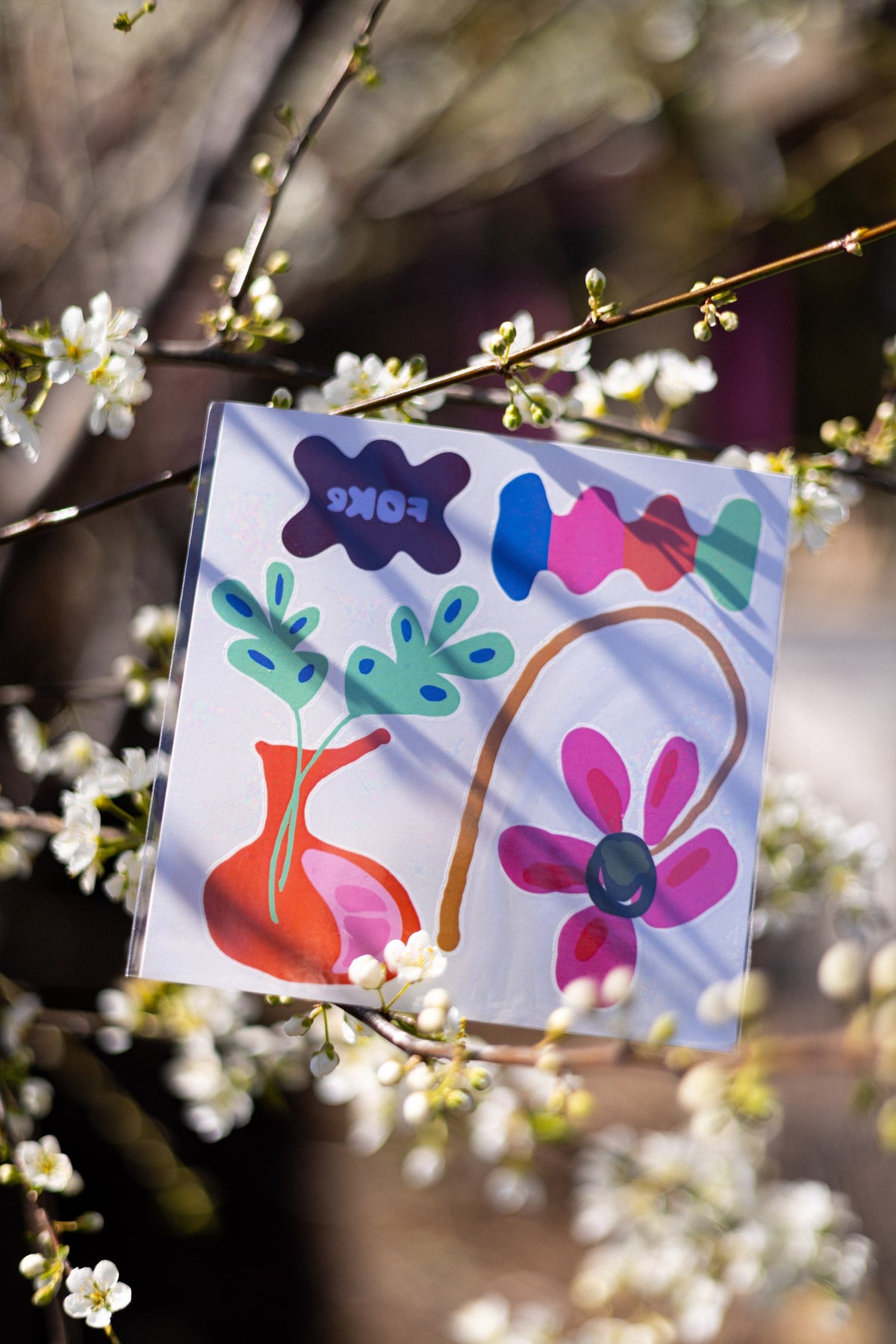 FOKE temporary tattoo sheet with a pink flower, orange vase and colourful shapes displayed among blossoms.