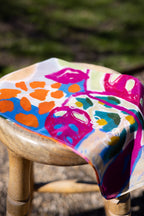 Offbeat cotton–silk scarf draped over a wooden stool, showing bold pink leaves and orange, blue and green artwork.