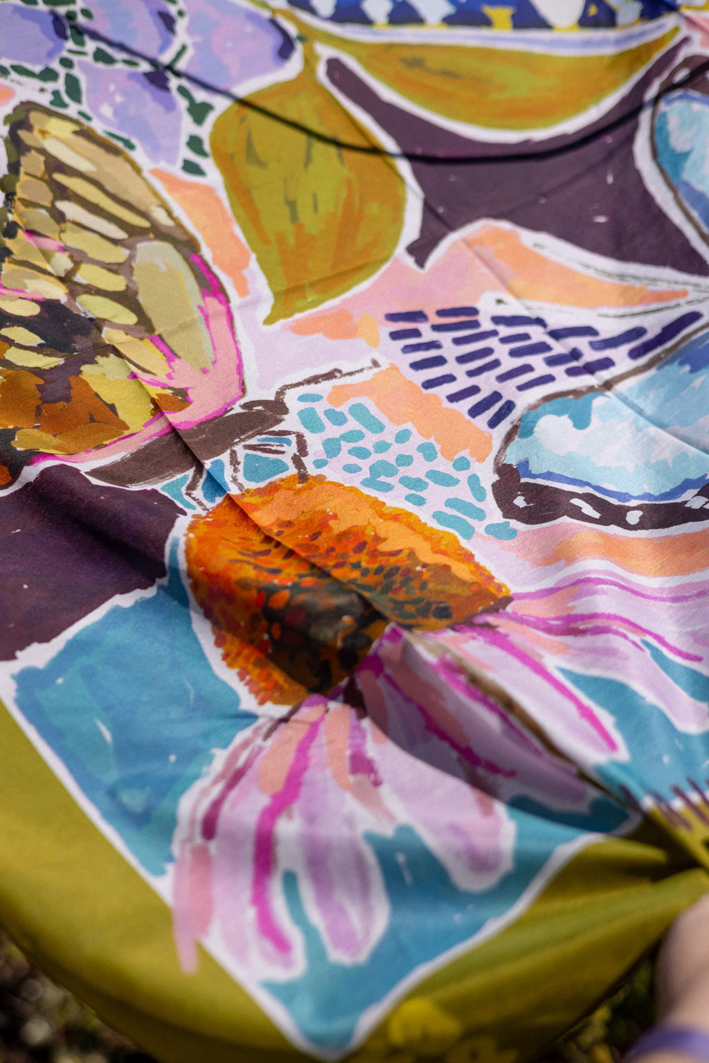 Wild Reverie scarf detail with a pink coneflower, butterfly wings and olive edging on lightweight cotton–silk fabric.