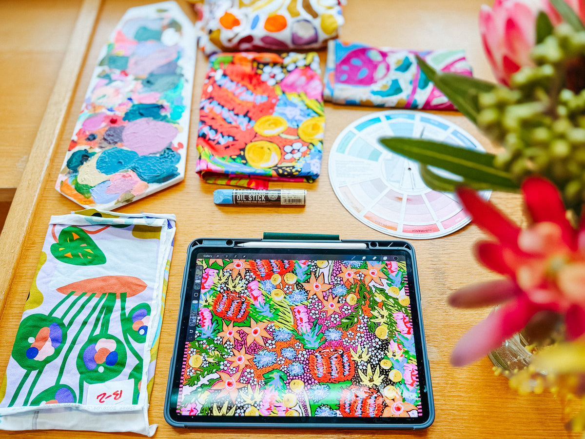Holly’s studio table with painted palettes, printed fabric, a colour wheel and an iPad showing a FOKE print in progress