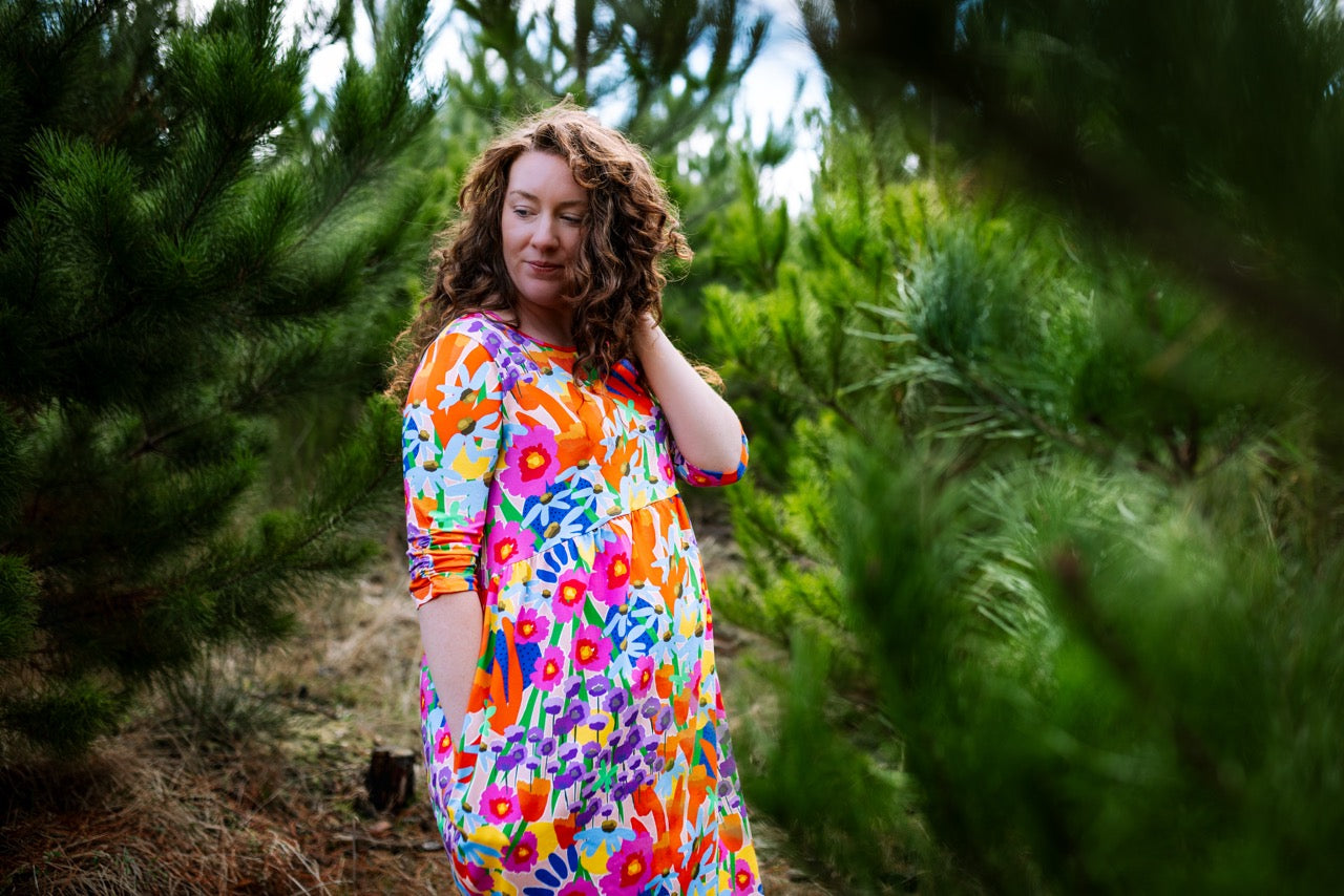 Woman in a colorful dress standing among trees. Print-led fashion dress, hand-drawn and consciously made.