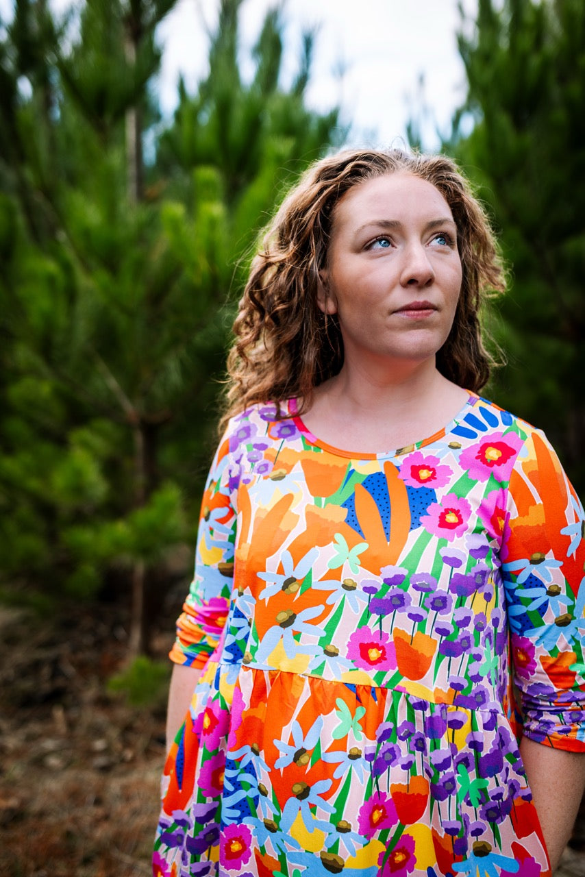 Woman wearing a colorful abstract floral dress standing in a forest. FOKE REN dress — print-led wearable art, bold and hand-drawn.