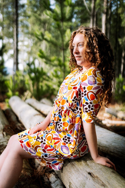 Women in a FOKE REN dress sitting on a log in the forest — print-led wearable art, bold and hand-drawn.