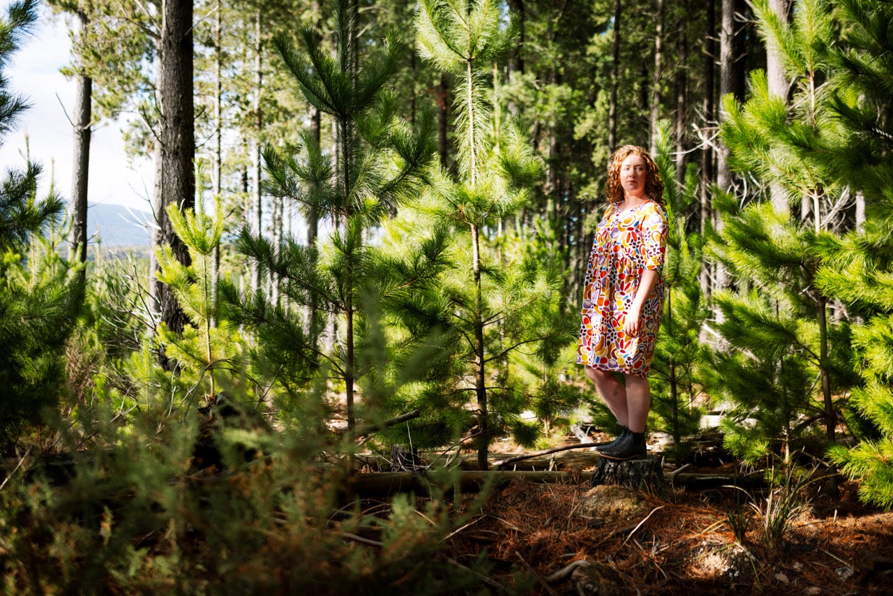 Woman in a colorful abstract dress standing in a forest. Joyful, expressive fashion — FOKE REN dress styled for bold women.
